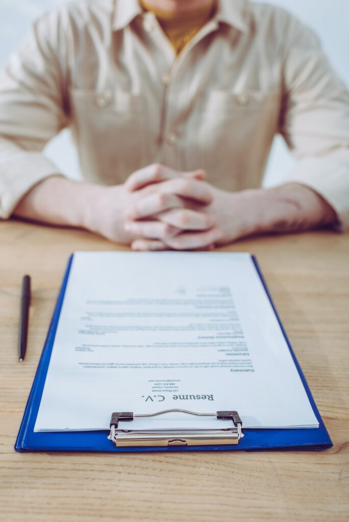 selective focus of clipboard with resume cv lettering near recruiter with clenched hands